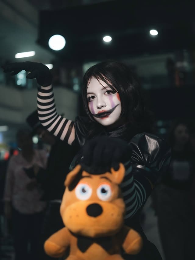 Cosplay con maquillaje teatral y peluche en un evento nocturno